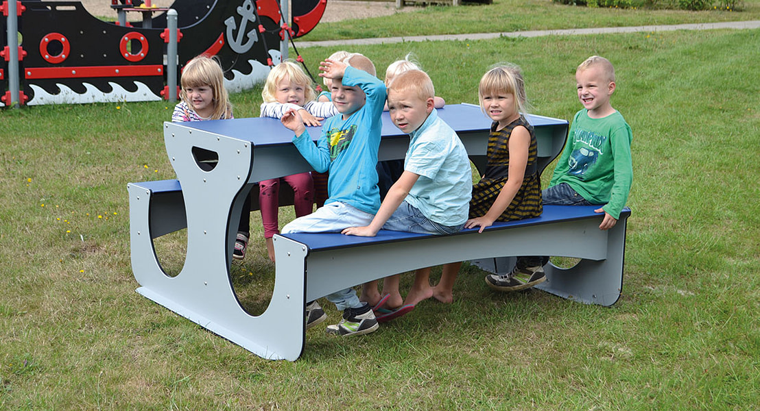 Børn sidder ved vedligeholdelsesfri bord bænkesæt på legeplads.