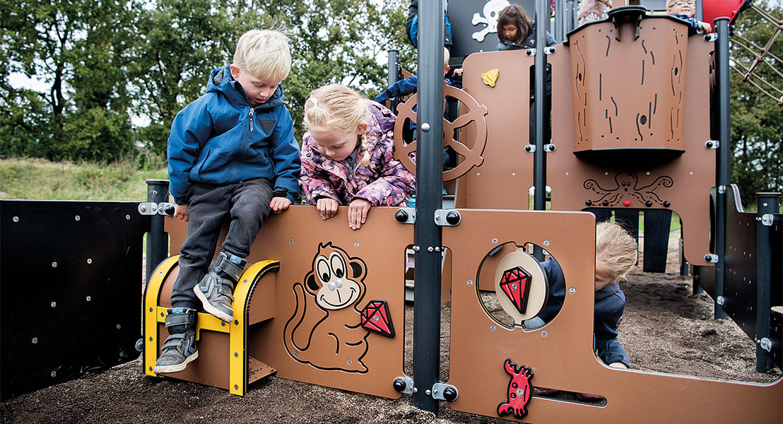 To børn leger på udendørs legeplads, designet som piratskib.