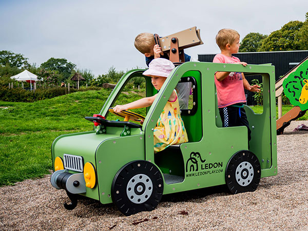 Legehuset på legepladsen er designet som en grøn bil, hvor tre børn leger.