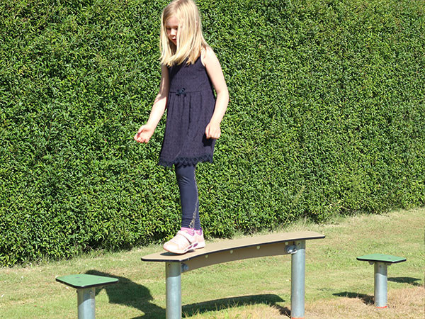 Pige balancerer på udendørs forhindringsbane.