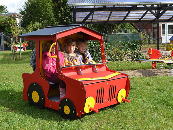 Legehuset på legepladsen er designet som en rød traktor, hvor tre børn leger.