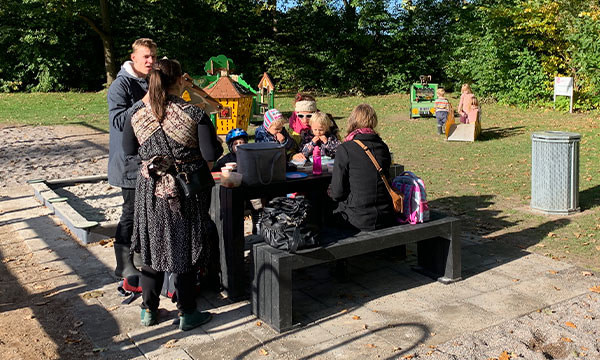 Børn og voksne nyder deres frokost på legepladsens bord bænkesæt.