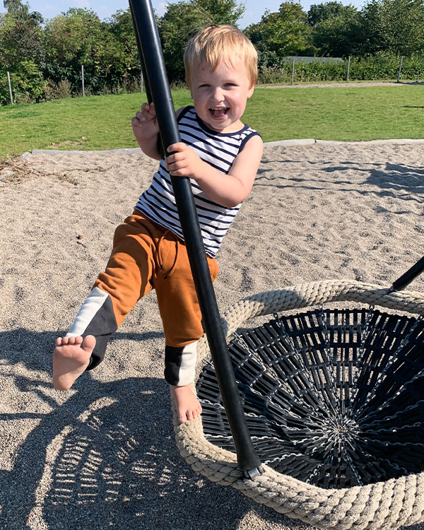 Lille barn hygger sig i fuglerede gynge på institutionenes legeplads.