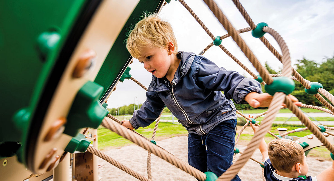 Dreng leger i klatretårn på legeplads.