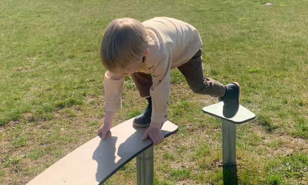 Dreng balancere på balancebom på legepladsens tarzan bane.