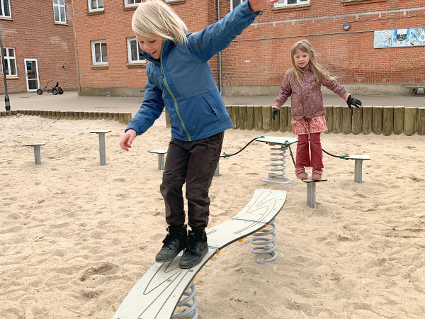 Dreng og pige balancerer på udendørs forhindringsbane i skolegården.
