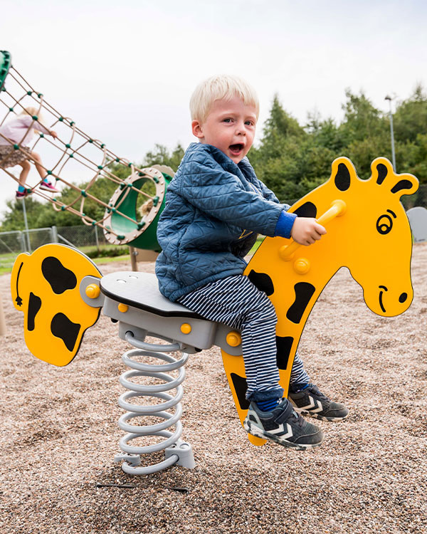Dreng vipper på et vedligeholdelsesfrit vippedyr, som ligner en giraf.